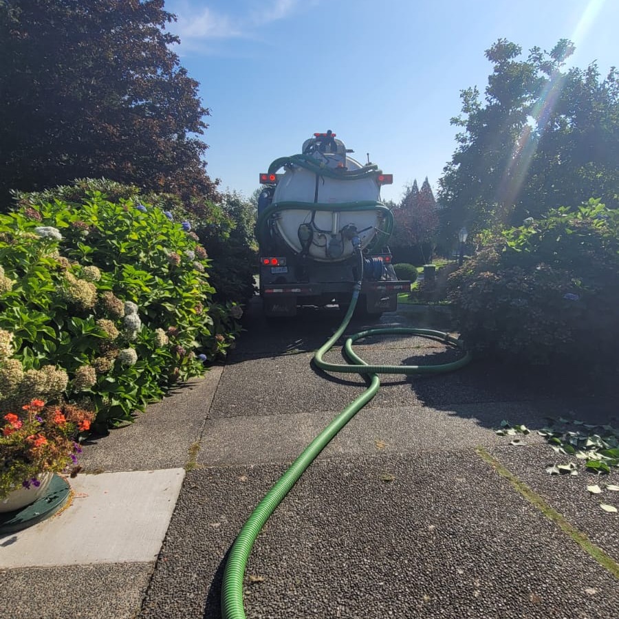 Vacuum truck and pumping hose set up on a landscaped residential driveway.